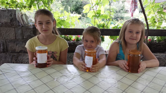 Petra, Paula, and Antonija at the Knežević family home displaying jars of honey harvested from their beehives.