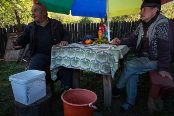 Two men chatting underneath a colourful sunshade in the garden of a private house, Mehedinti plateau geopark, Isverna, Romania