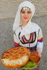 Young woman in Balkan dress offering bread and honey at the Celebration of the opening of a new Tahini-production factory in Kondovo village, Eastern Rhodope mountains, Bulgaria