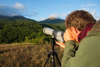 Man bearwatching with fieldscope at sunrise from lookout point in the Central Apennines rewilding area, Italy. 