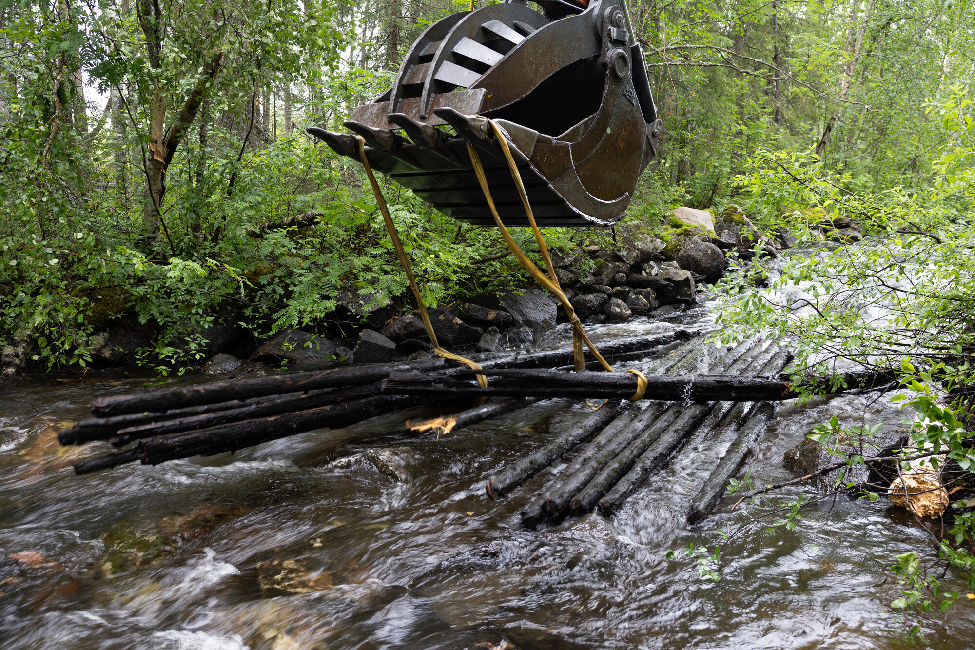 Excavator bucket pulling up artificial flooring on riverbed, Swedish Lapland.