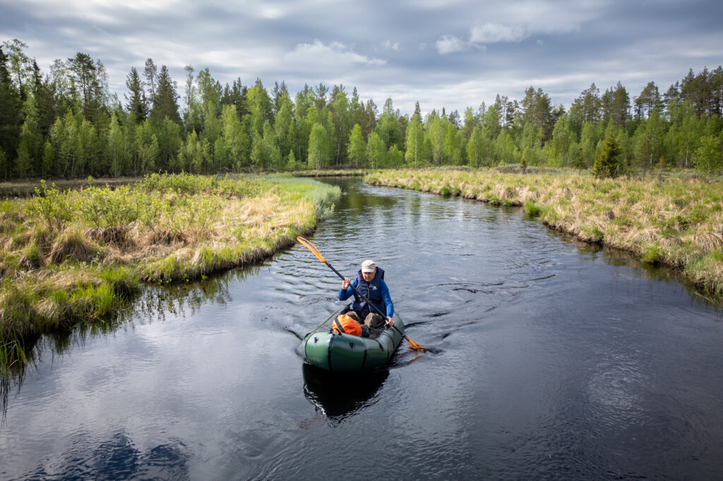 A person packrafting down the Hjuksån river system in the Nordic Taiga, Sweden.